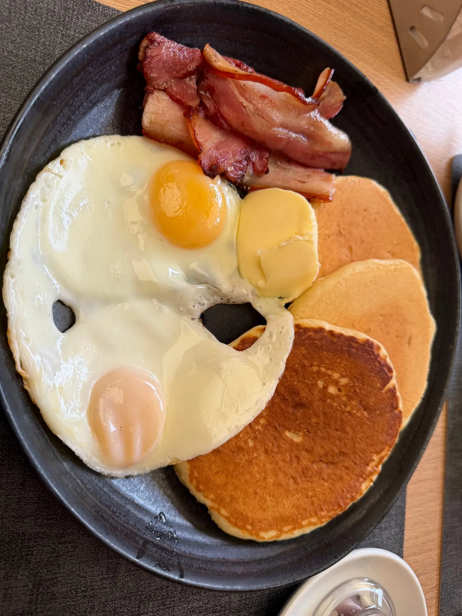 Ovos estrelados, bacon e panquecas com manteiga numa frigideira preta