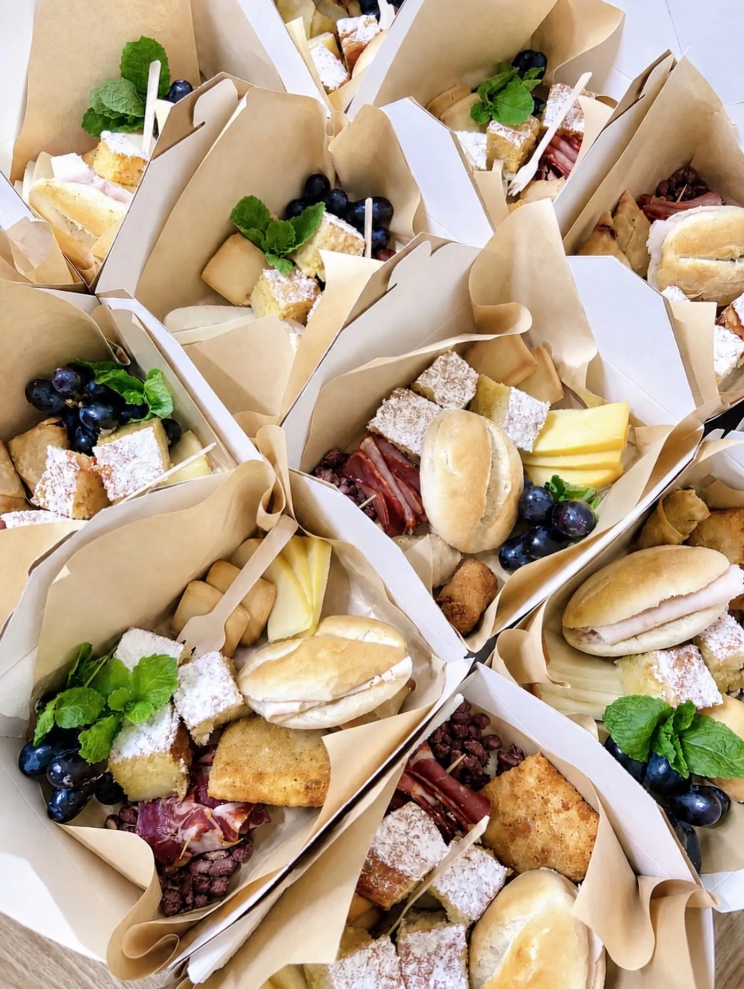 Brunch boxes com pãezinhos, queijo, fruta, enchidos e bolos, prontas para um evento